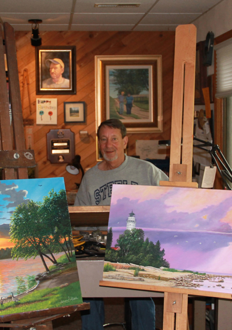 Gregory D. Steele in his workshop, displaying two of his paintings